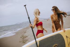 Two young women with paddle board on the beach on a summer day photo