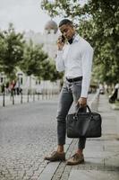 Young African American businessman using a mobile phone while waitng for a taxi on a street photo