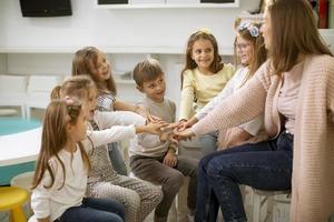 lindos niños en edad preescolar se dan la mano con su maestra de guardería foto