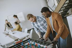 Young casual multiethnic business people playing table football and relaxing at office photo