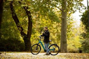 Apuesto joven con bicicleta eléctrica en el parque de otoño foto
