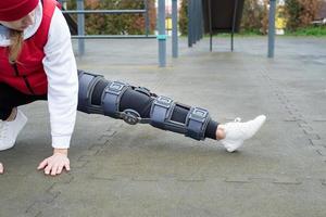 Woman wearing knee brace or orthosis after leg surgery working out in the park photo