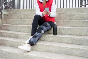 Woman wearing knee brace or orthosis after leg surgery, sitting on stairs ourdoors photo
