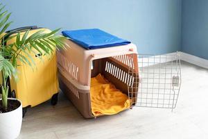 Opened plastic pet carrier or pet cage and yellow suitcase on the floor at home, copy space photo