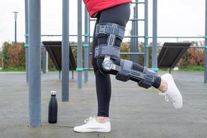 mujer con rodillera u ortesis después de una cirugía de piernas haciendo ejercicio en el parque foto