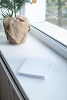 Blank book for mockup design on windowsill, christmas tree behind photo