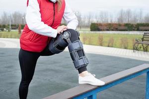 Woman wearing knee brace or orthosis after leg surgery working out in the park photo