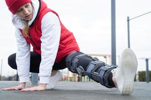 Woman wearing knee brace or orthosis after leg surgery working out in the park photo