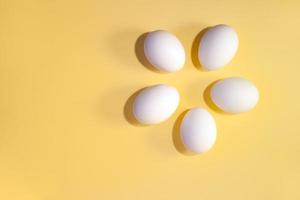 Five white eggs are lying in circle on a yellow background with copy space. photo