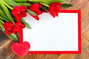 White blank sheet in red frame, red tulips and plush heart on rustic wooden background. photo