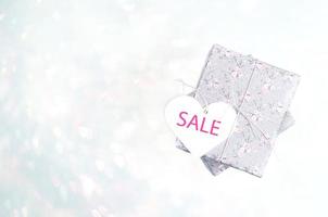 Gift boxes wrapped with grey paper with floral pattern and white heart with word SALE on light blue bokeh backdrop. photo