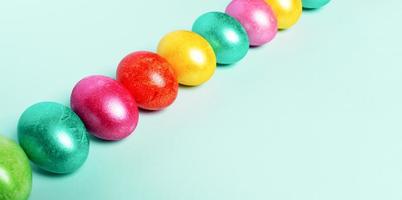 Diagonal row of brightly multicolored painted Easter eggs on trendy Neo Mint pastel background. Easter festive banner. photo