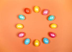 Multicolored glossy Easter eggs laid out in circle on trendy orange background. Creative festive Easter backdrop. photo