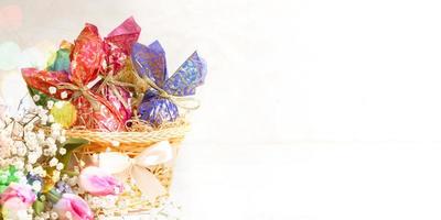 Easter banner with basket of eggs wrapped in colorful paper, flowers, bokeh lights. Copy space. photo