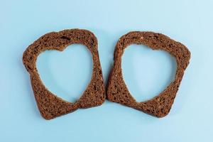 Two rye bread slices with carved holes of heart shape in them on light blue background. Top view, close-up. photo