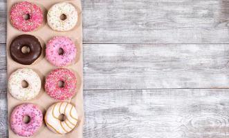 Eight traditional doughnuts with multicolored glaze on wrapping paper on white painted wooden table with copy space. photo