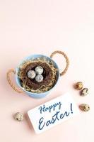 Nest of quail eggs in small bucket, note Happy Easter on pastel pink vertical backdrop. photo