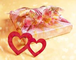 Trendy wrapped in Furoshiki technique gift box with flowers Alstroemeria and two red wooden hearts on yellow with bokeh. photo