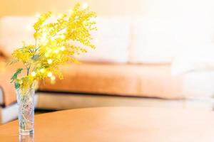 Fresh spring mimosa branch in vase in table in modern minimal living room with sofa. Copy space. photo