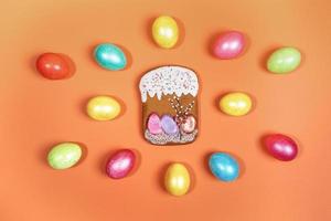 Festive Easter composition of bright multicolored Easter eggs and gingerbread Easter cake on orange background. photo