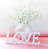White letters LOVE with art round vase of white gypsophila flowers on pink-white. Close up. photo