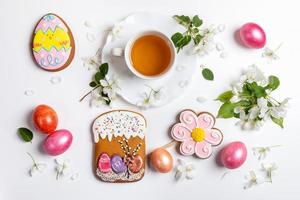 Easter festive arrangement of cup of tea, white Apple tree twigs, colored eggs, gingerbreads on white background. photo