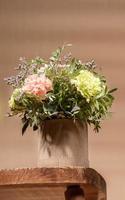 Eco friendly composition with flowers bouquet in DIY carton vase standing on old wooden table on beige with copy space. photo