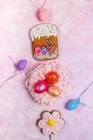 Easter festive vertical background with colored eggs in decorative nest and ornamental Easter eggs, Easter gingerbreads on pink background. photo