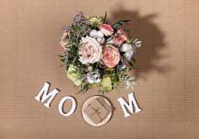 Festive composition for Mother's day with flowers bouquet, white letters MOM, diy gift box on beige cardboard backdrop. photo