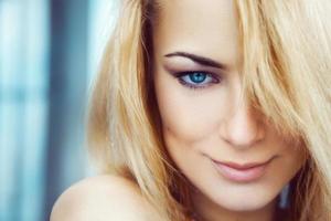 Close up photo of cute young adult blonde woman with blue eyes. Looking at camera and smiling