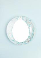 Easter creative festive minimal layout with copy space in egg shape on plate on center of light blue backdrop. photo