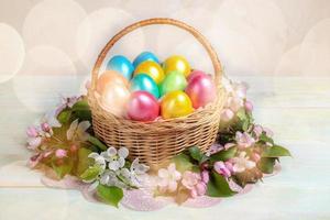 Easter composition of basket of painted Easter eggs and sprigs Apple trees around it on wooden backdrop with bokeh. photo