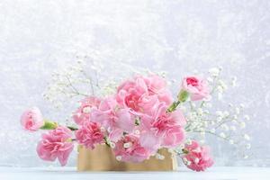 Pink carnations and white gypsophila flowers on wooden stand on light grey. Mother's Day card. photo