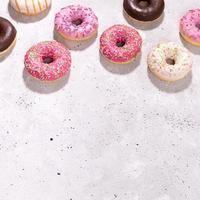 Set of traditional doughnuts with multicolored glaze laid out on concrete background. Copy space, selective focus. Square photo with shadows.