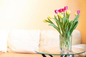 tulipanes en jarrón en mesa de cristal en salón con sofá. 8 de marzo, cumpleaños, concepto de día de san valentín foto