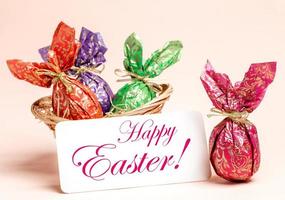 Easter card - basket of eggs wrapped in color paper on pastel pink, note with words Happy Easter. photo