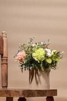 Ecological holiday geometric composition with flowers bouquet in DIY cardboard vase and old wooden chair on beige. photo