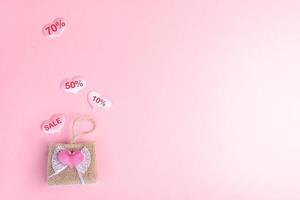 concepto de venta del día de san valentín. bolso de mimbre decorativo y corazones con porcentajes de descuento sobre fondo rosa. foto