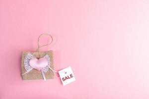 pequeño bolso de mimbre decorativo y tarjeta de papel blanco con venta de palabras sobre fondo rosa. concepto de venta del día de san valentín. foto