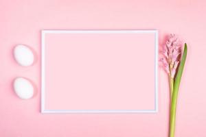 Easter minimal concept with white frame, two white eggs and hyacinth flower on pastel pink with copy space for text. photo