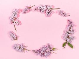 Creative floral spring background with twigs of lilac laid out in oval with copy space in it on trendy pink backdrop. photo