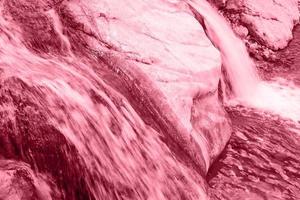 Close up small waterfall on a stone mountain river toned in color 2023 Viva Magenta. photo