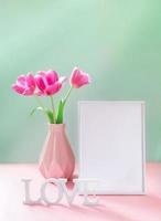 Pink tulips in vase, empty white frame, white letters LOVE on pastel pink green backdrop. Mock up. photo