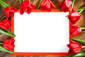 White blank sheet in red frame with copy space and red tulips around it on wooden background. photo