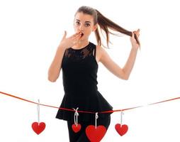 beautiful young girl in a black dress stands near the tape with cards in the shape of hearts and surprise keeps hand near mouth photo