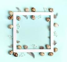 marco cuadrado blanco con huevos de codorniz, plumas, flores blancas de gypsophila en azul claro. tarjeta de pascua foto