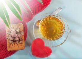 Valentine's day morning tea. Cup of tea, plush heart, gift box on light blue backdrop and palm leaves shadows overlay. photo