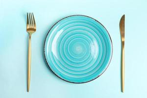 Empty blue round ceramic plate with golden cutlery on light blue backdrop. Top view. photo