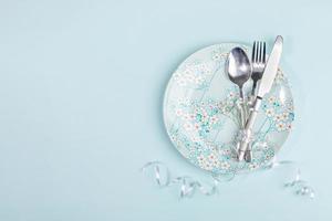 Top view Easter table setting with flatware on light blue plate with spring flowers decor on pastel blue. Copy space. photo