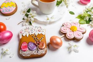 Close-up Easter festive gingerbreads and colored eggs with cup of tea and white Apple tree twigs on white background. photo